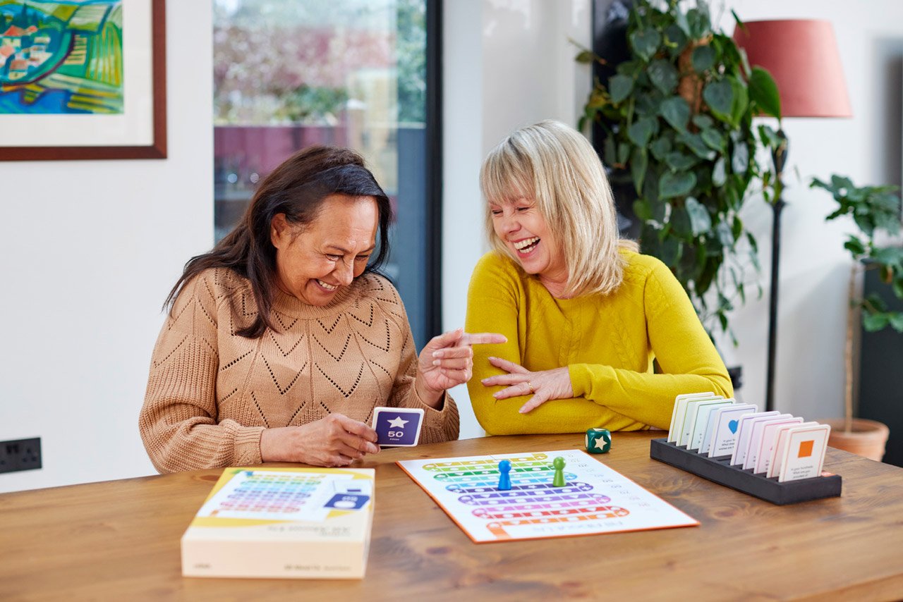 Two women playing a dementia-friendly board game designed to spark conversation.