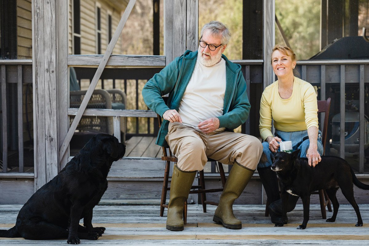 A man and woman sit on decking with their two black dogs. This is a great activity for dementia.