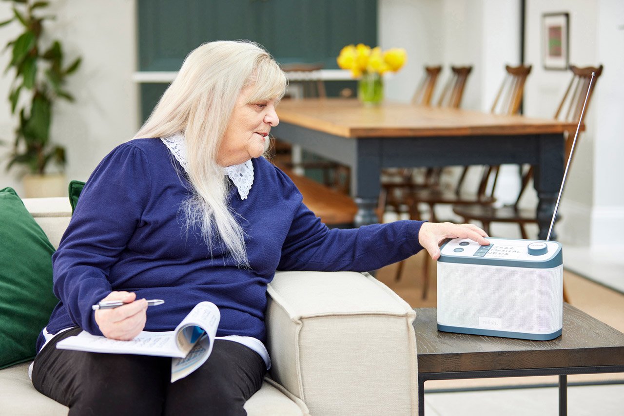 Relish dementia-friendly radio being enjoyed by a woman sitting on the sofa completing a crossword puzzle.